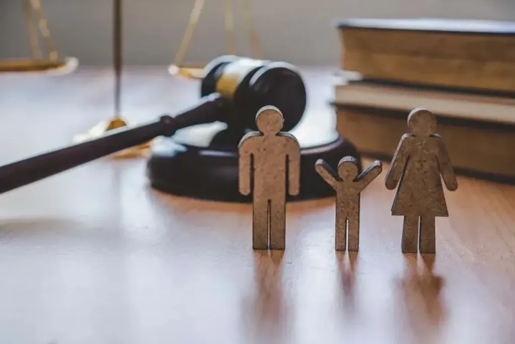 Wooden cutouts of a family (man, woman, and child) standing in front of a gavel and legal books, symbolizing family law, child custody, and divorce proceedings.